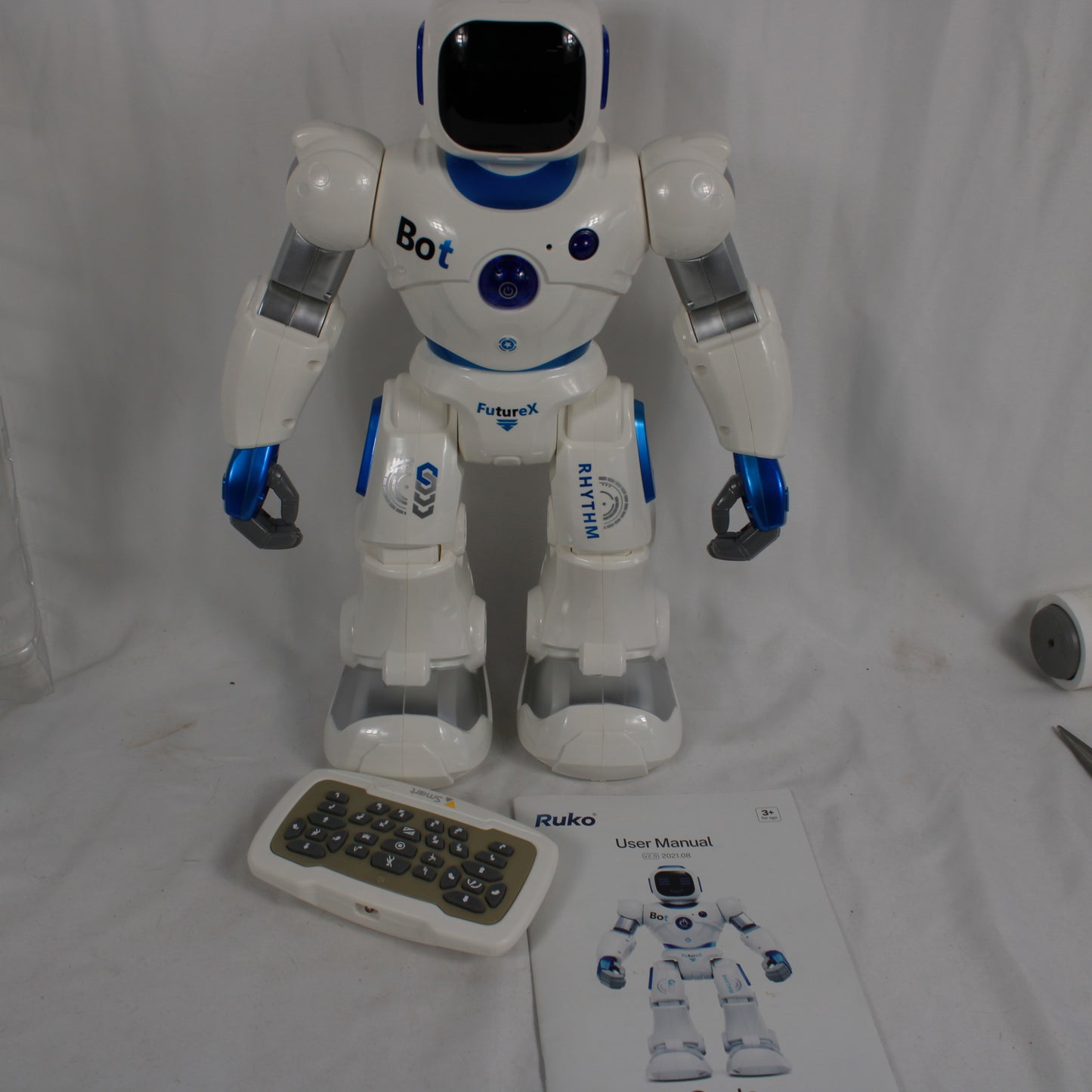 White robot with blue accents on a white background, accompanied by a remote control and user manual.