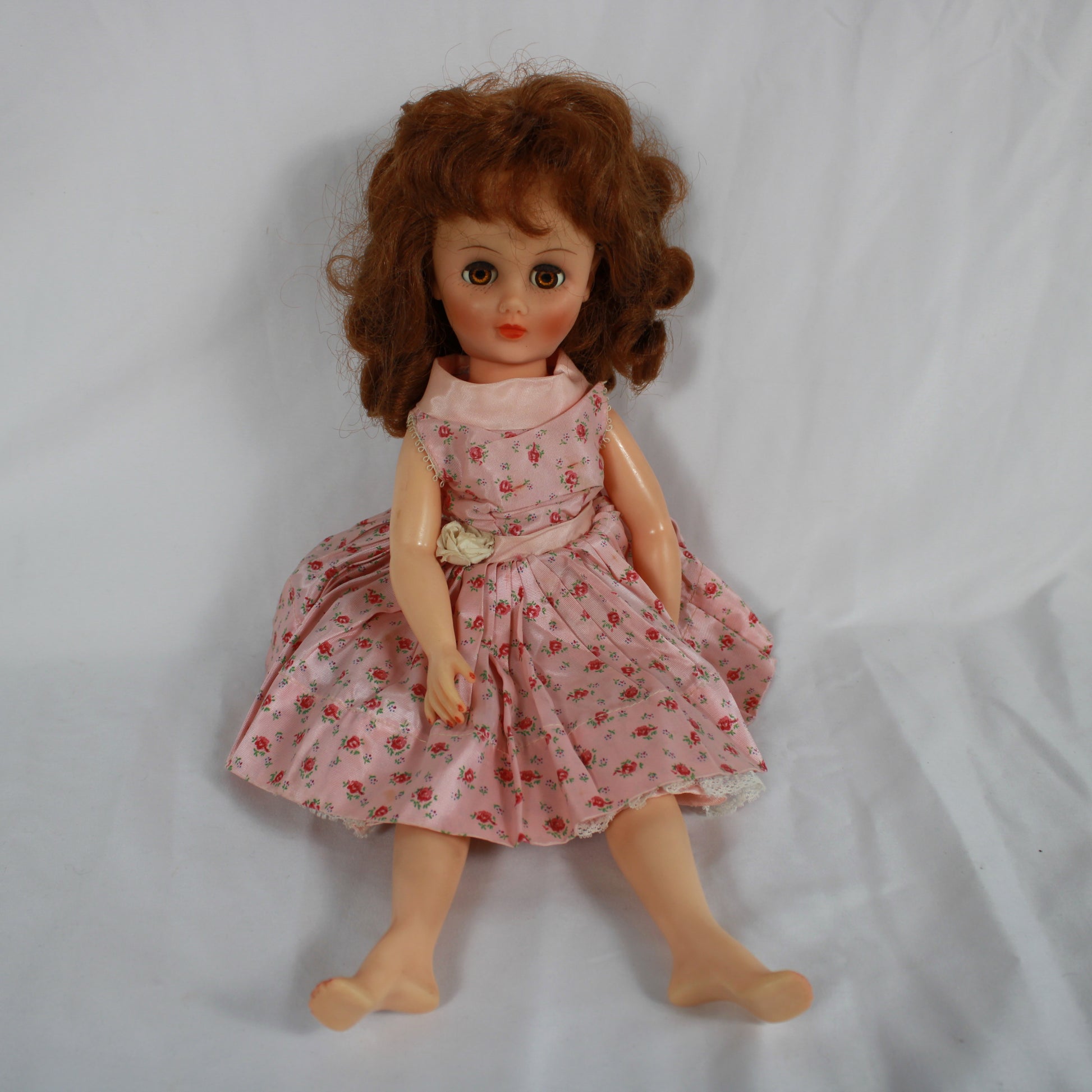 Vintage doll with a pink floral dress sitting on a plain background