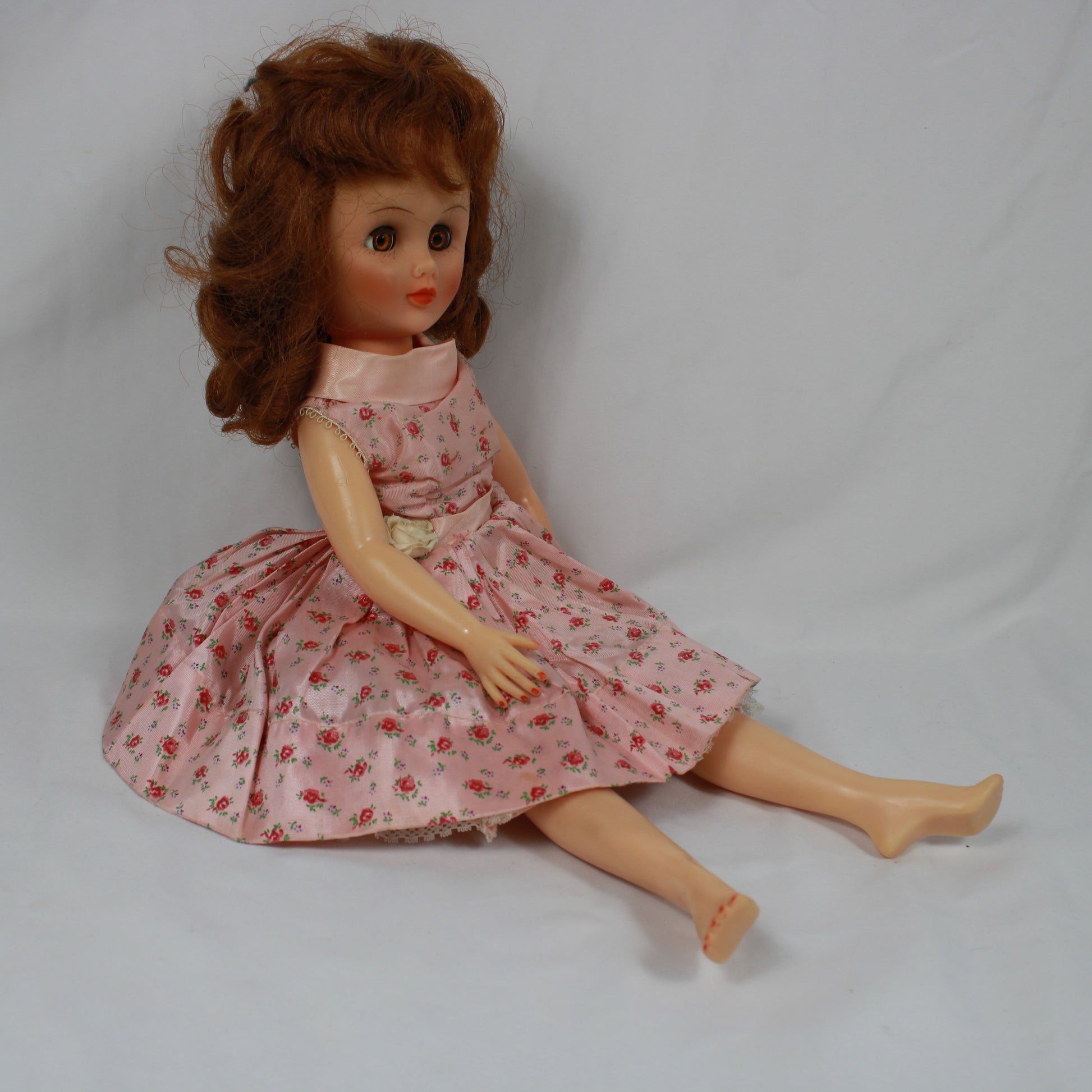 Vintage doll with a pink floral dress sitting on a plain background