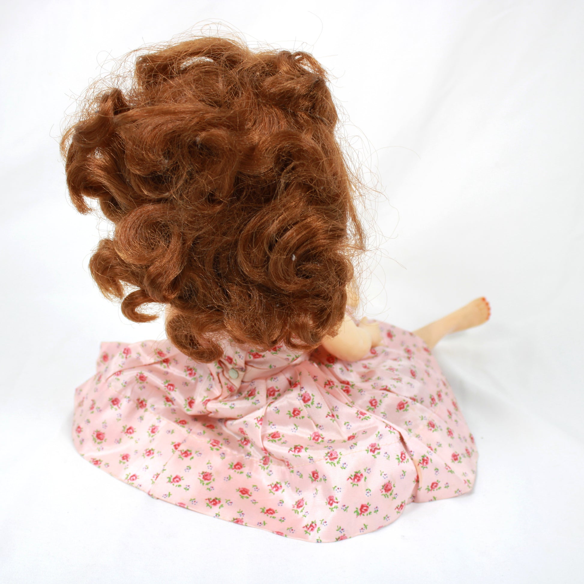 Vintage doll with a pink floral dress sitting on a plain background