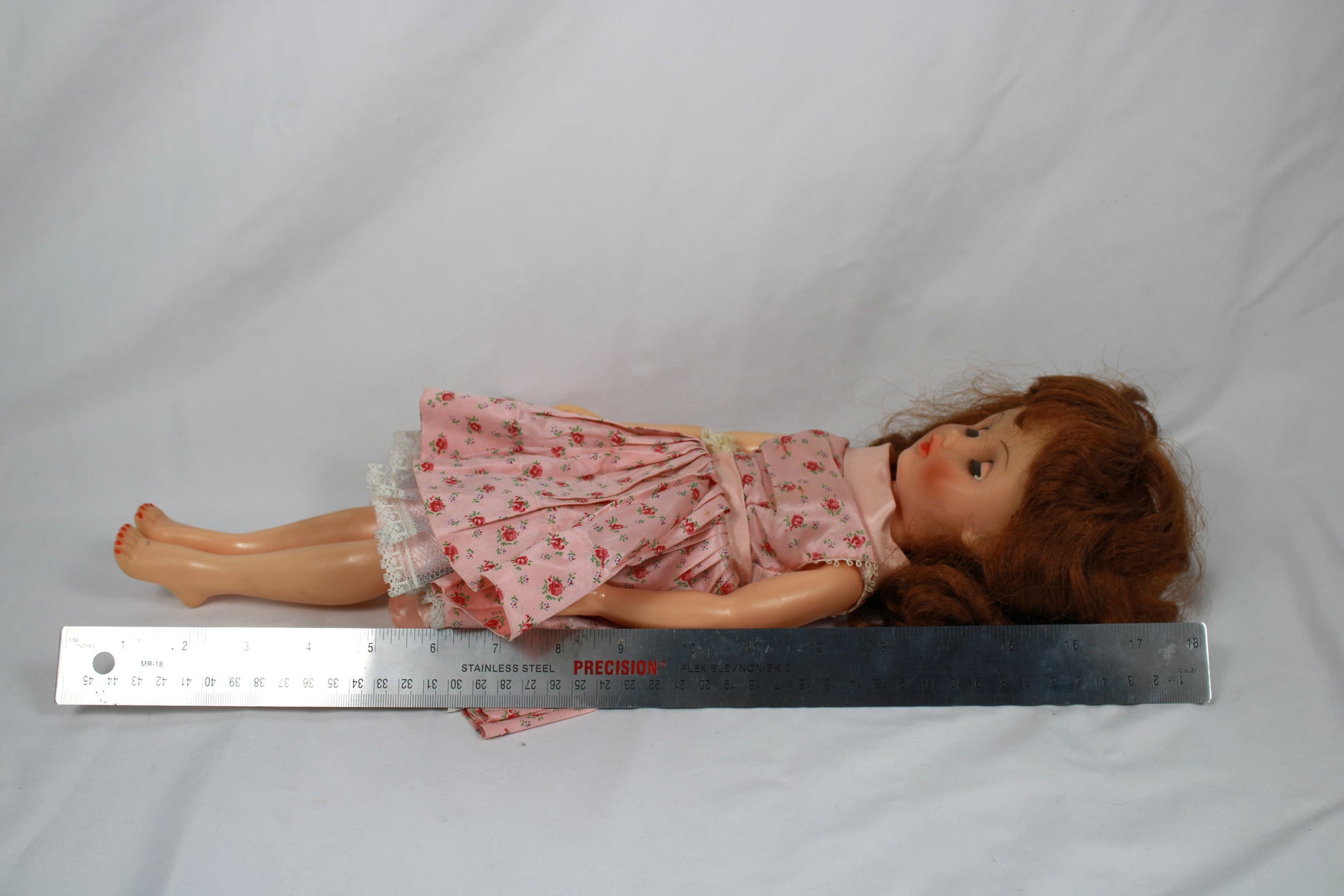Vintage doll with a pink floral dress sitting on a plain background