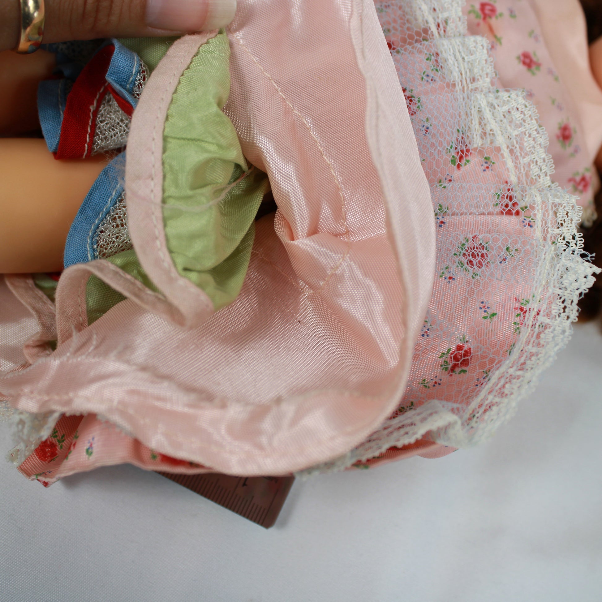 Vintage doll with a pink floral dress sitting on a plain background