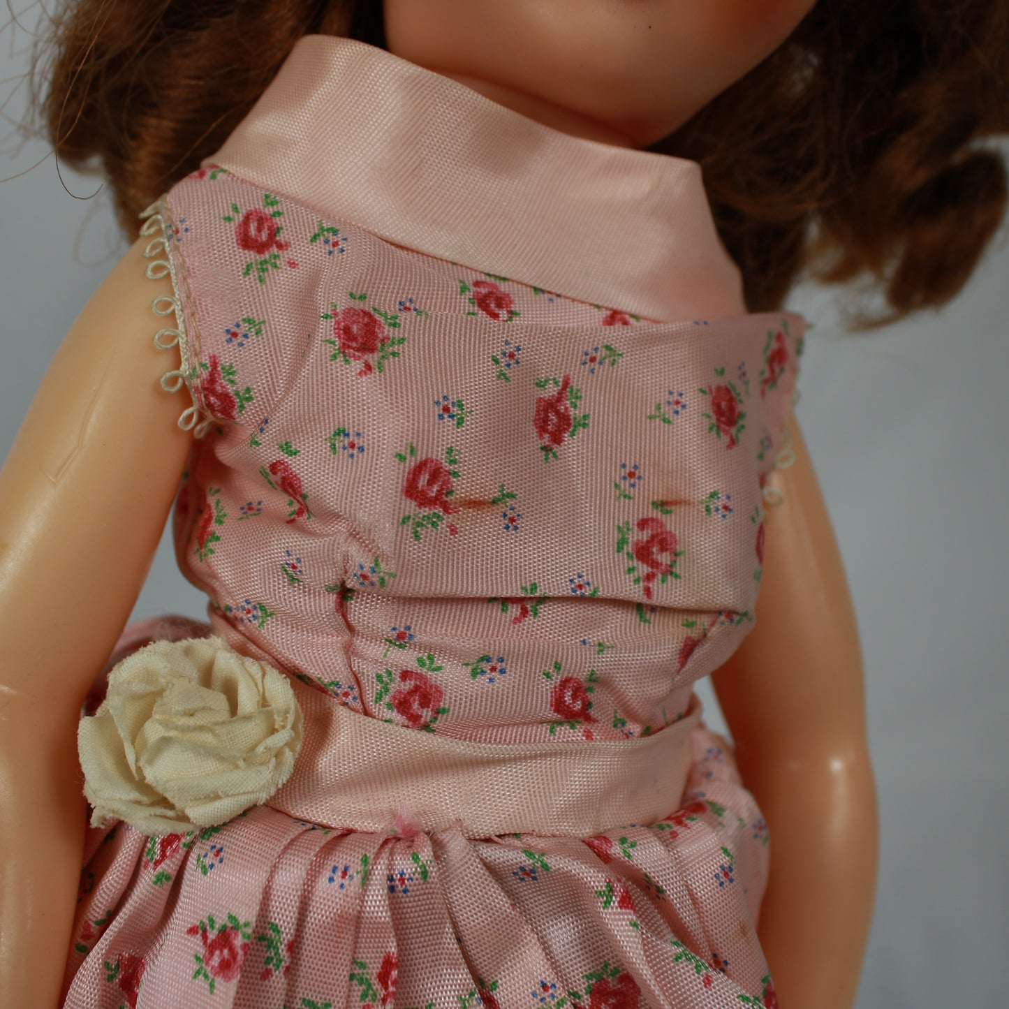 Close-up of a doll wearing a pink floral dress with a white flower accessory.