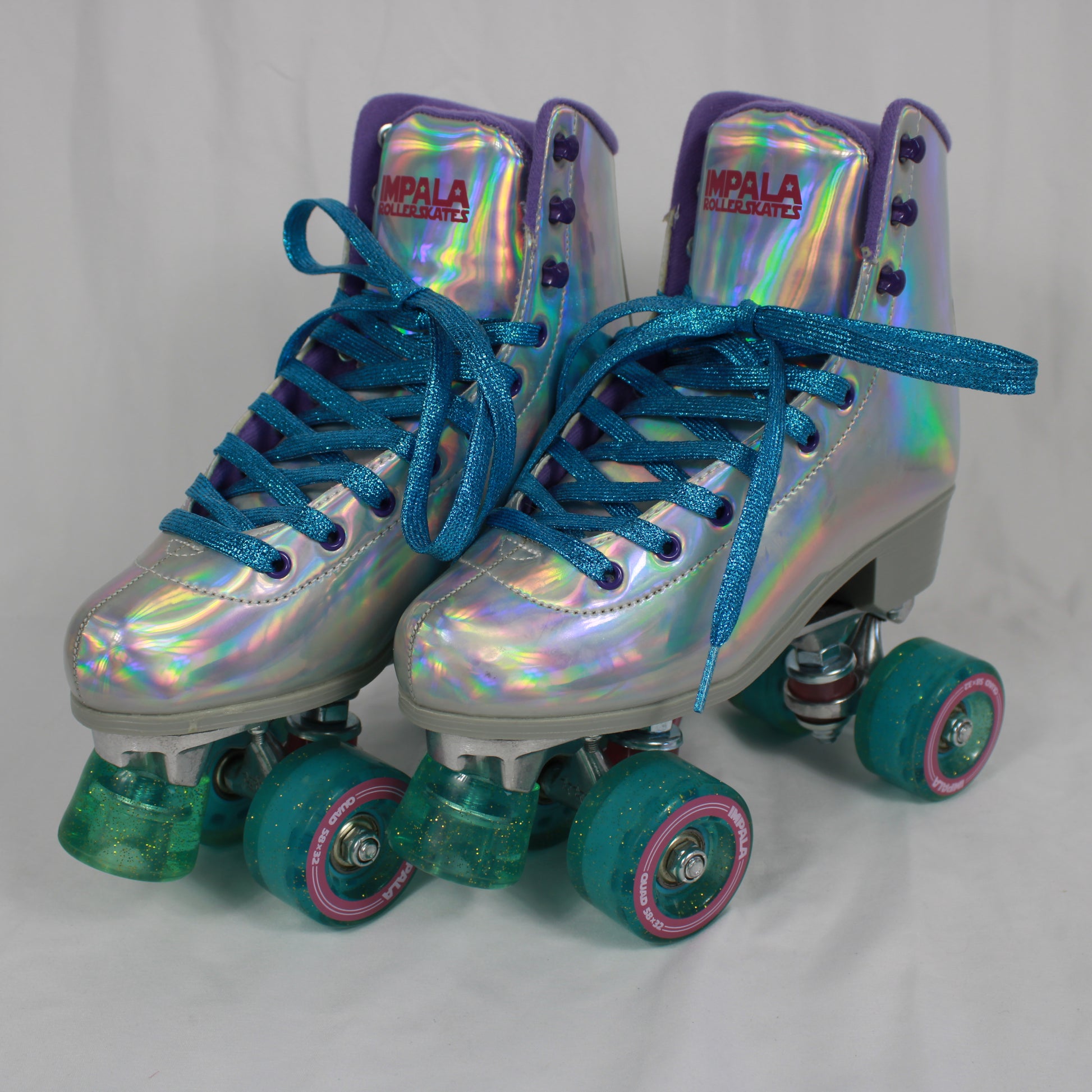 Pair of iridescent roller skates with blue laces on a light gray background