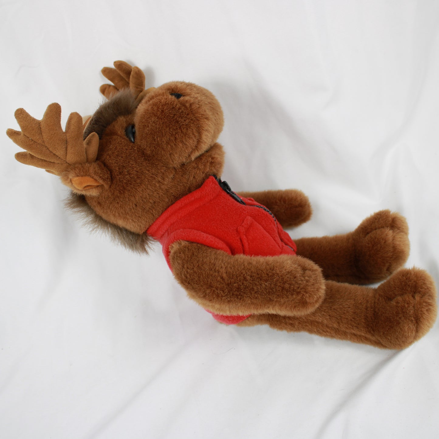 Plush moose toy wearing a red vest and hat with a Canadian flag, on a white background.