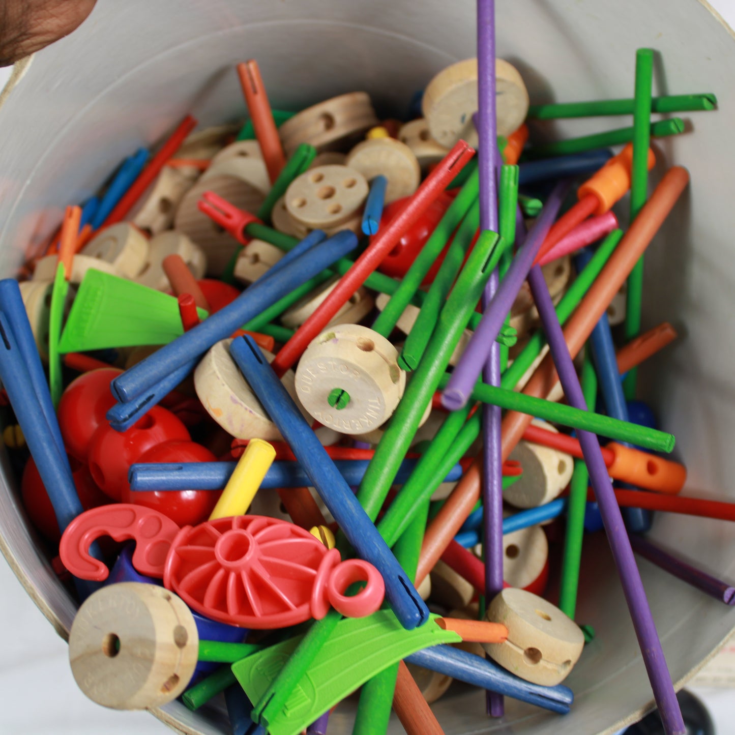 Assorted colorful plastic craft sticks and buttons in a white container