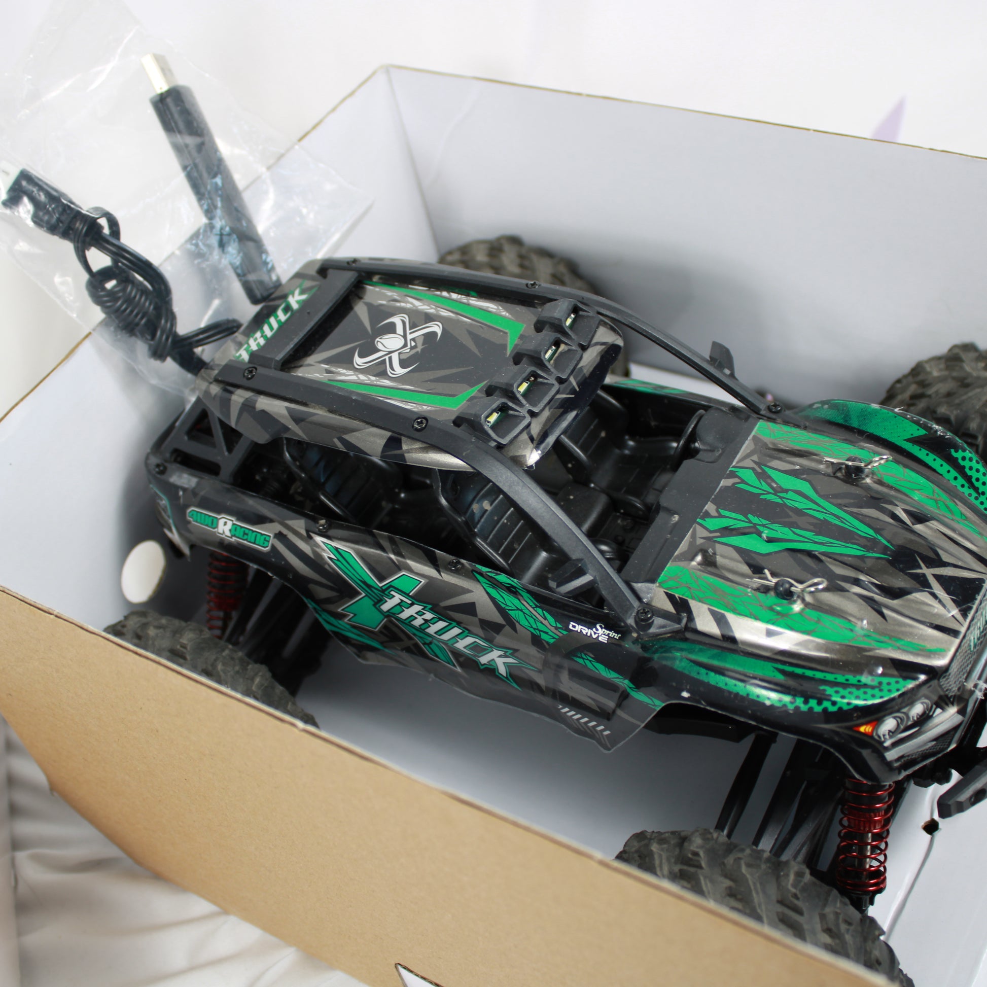 Green and black toy truck inside a cardboard box on a white surface