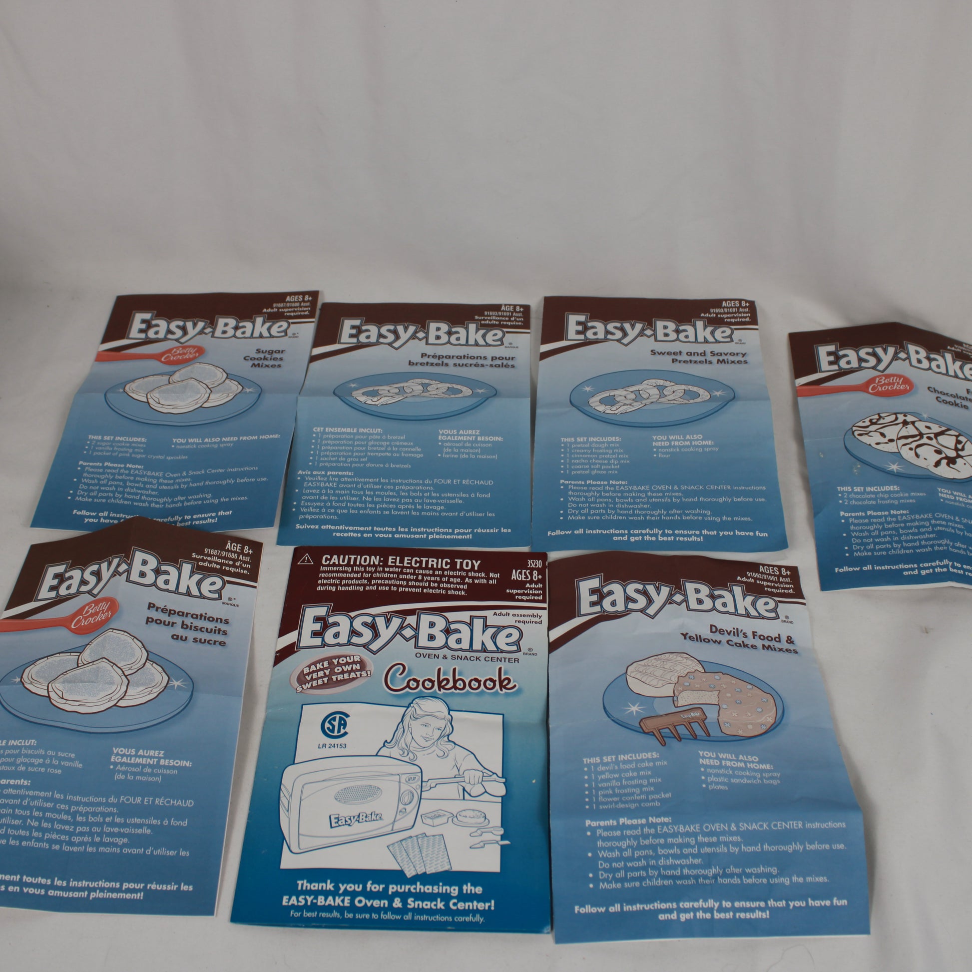 Collection of Easy-Bake Oven accessories and cookbook on a white background