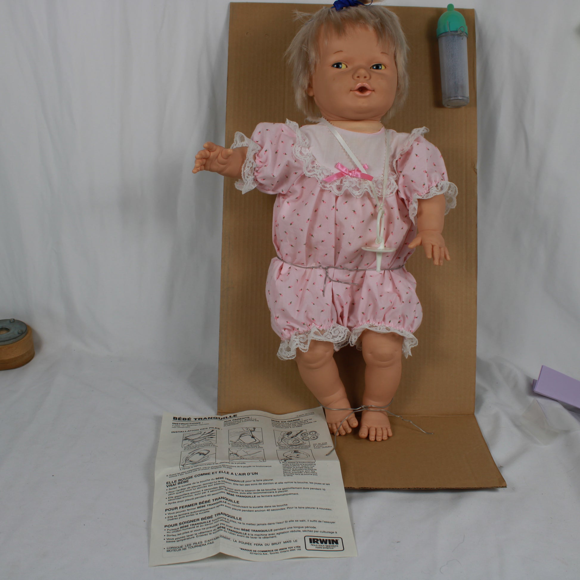 Vintage doll with pink outfit on a cardboard stand with a paper attached, on a white background.
