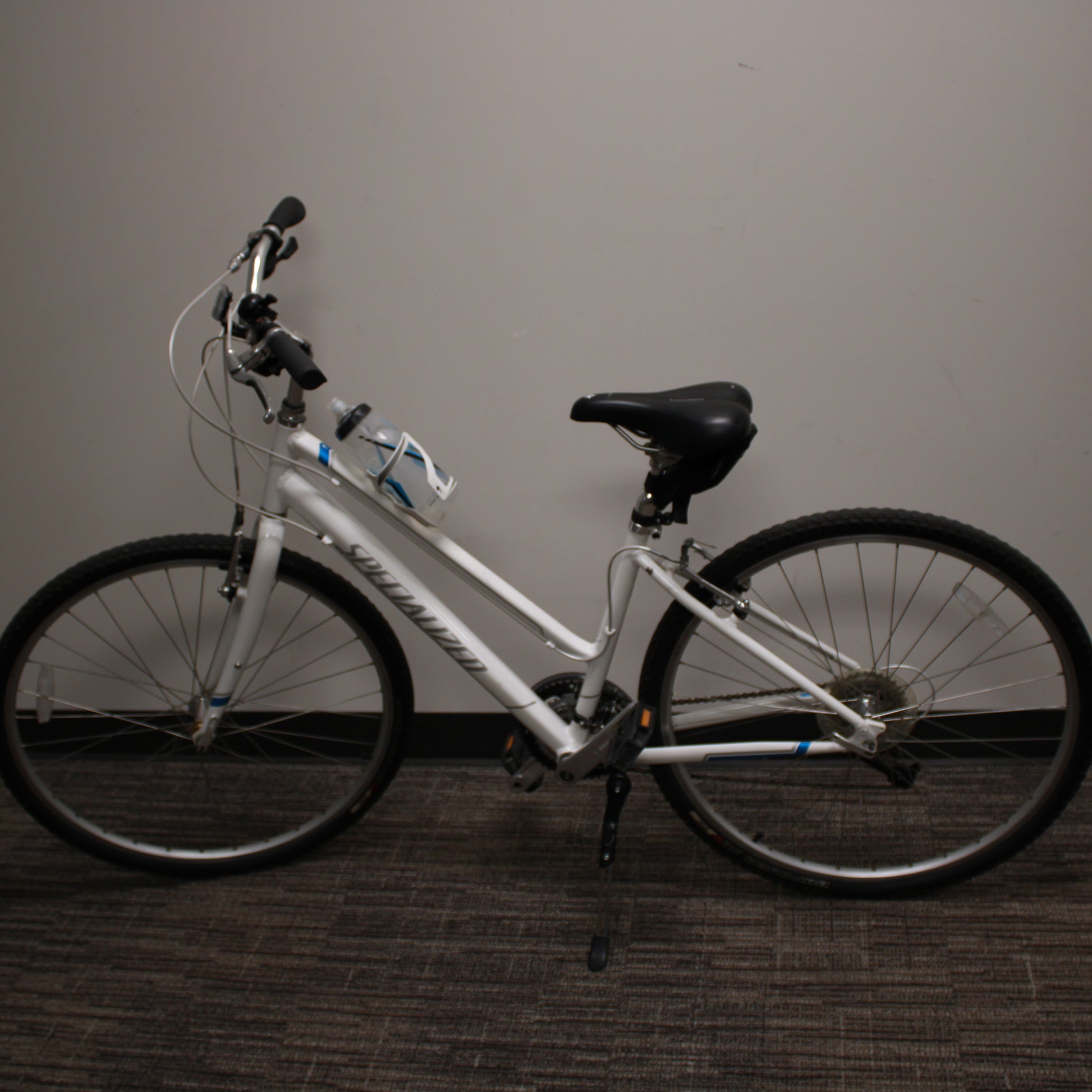 White bicycle with black seat and tires against a plain wall.