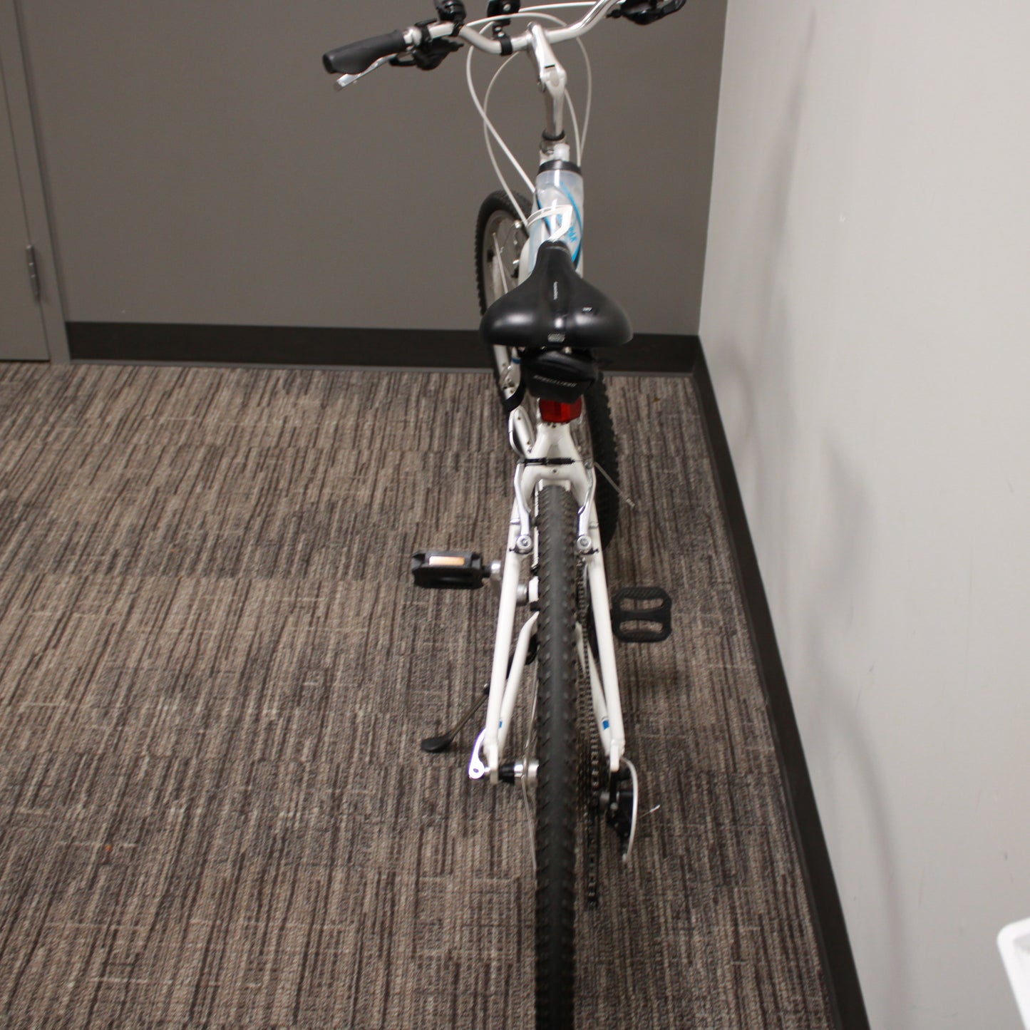 White bicycle on a carpeted floor against a gray wall