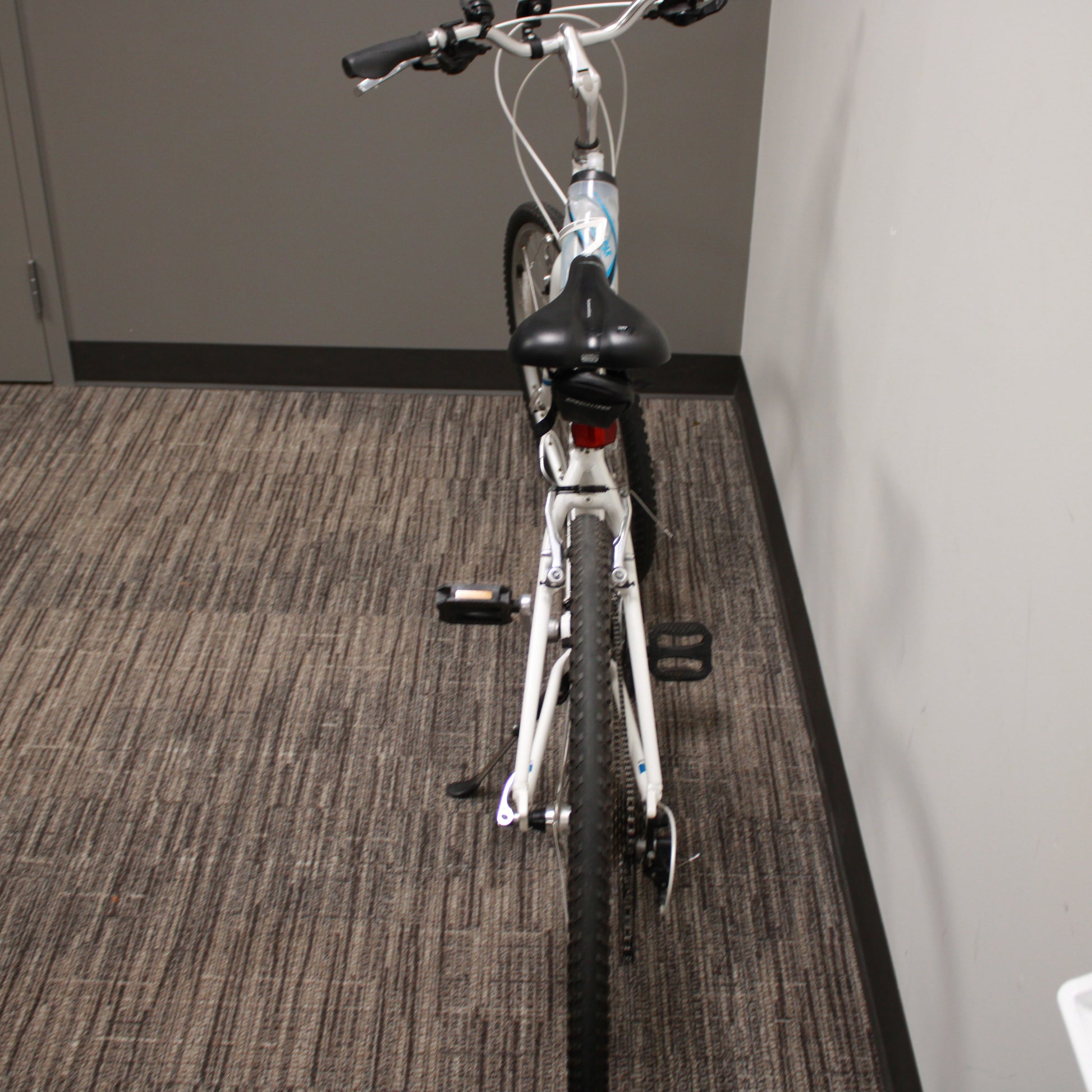 White bicycle on a carpeted floor against a gray wall