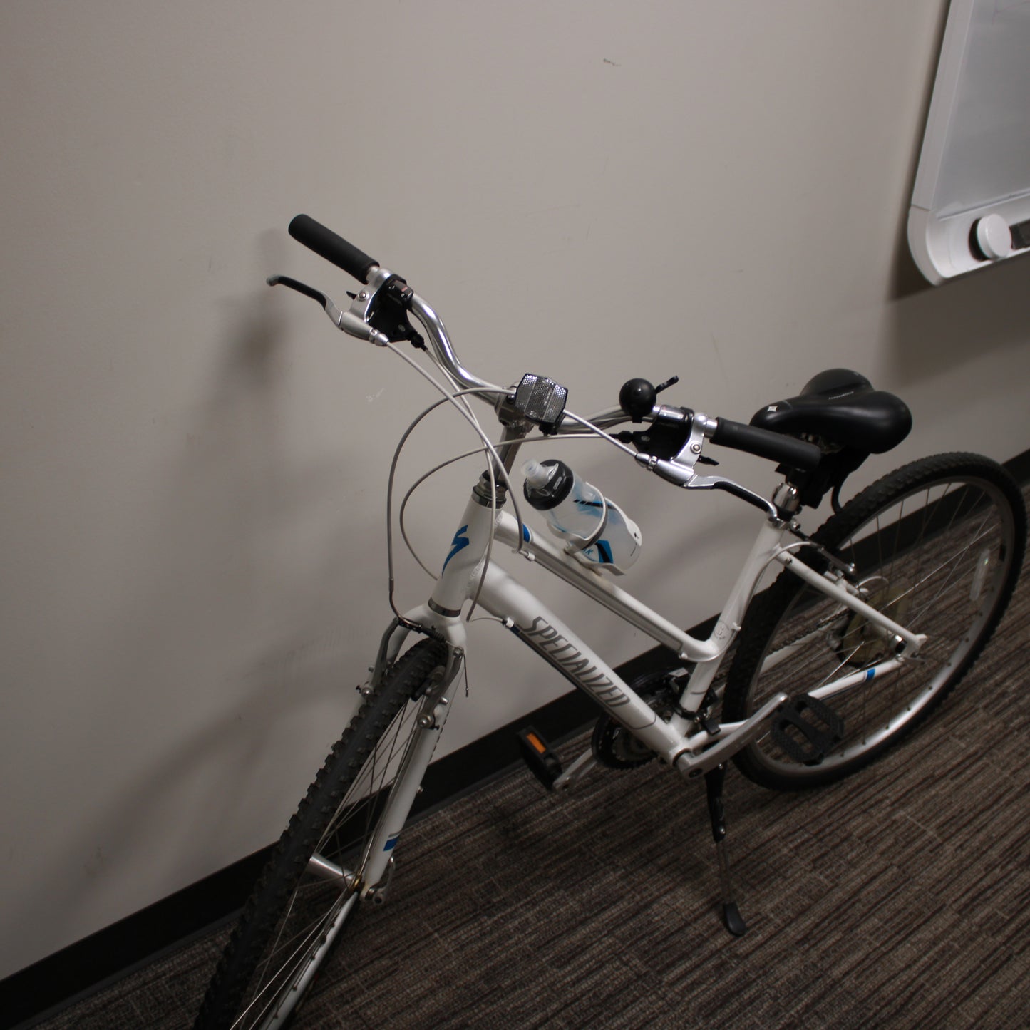 White bicycle with black seat and tires against a plain wall.