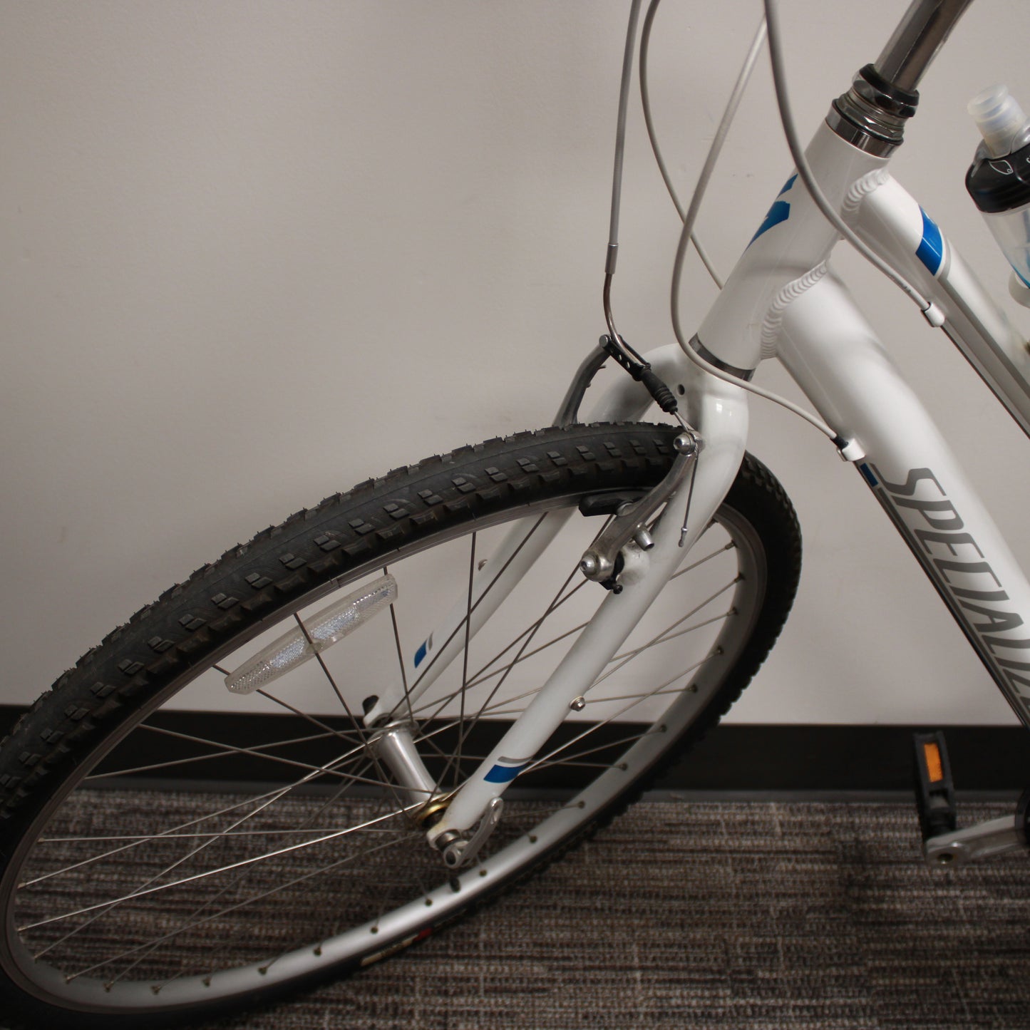 White bicycle with black tire on a carpeted floor against a plain wall