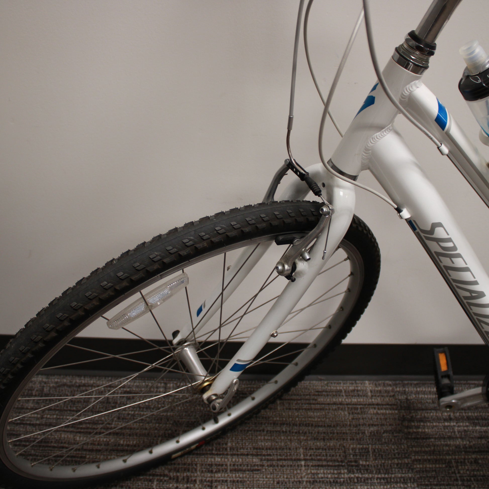 White bicycle with black tire on a carpeted floor against a plain wall