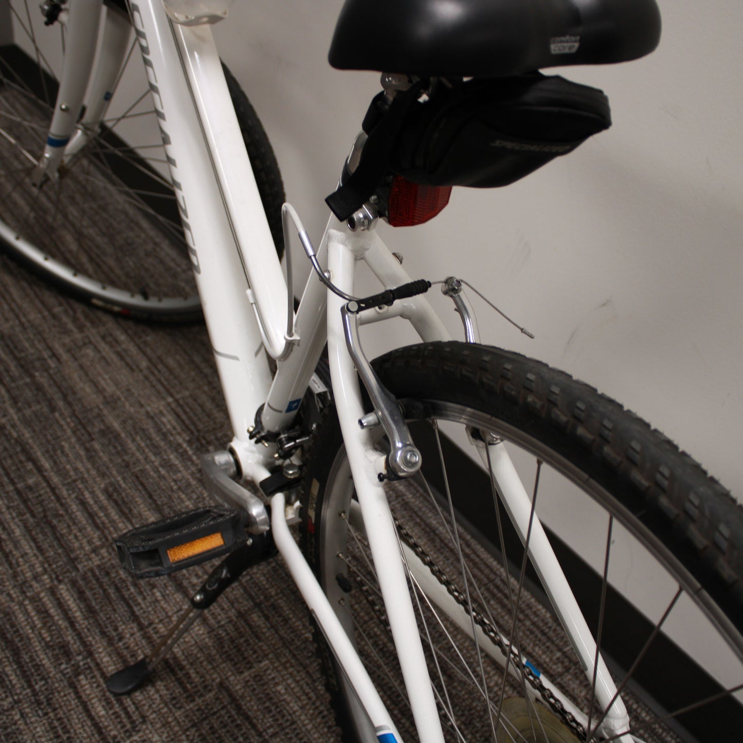 Close-up of a white bicycle with black seat on a carpeted floor.