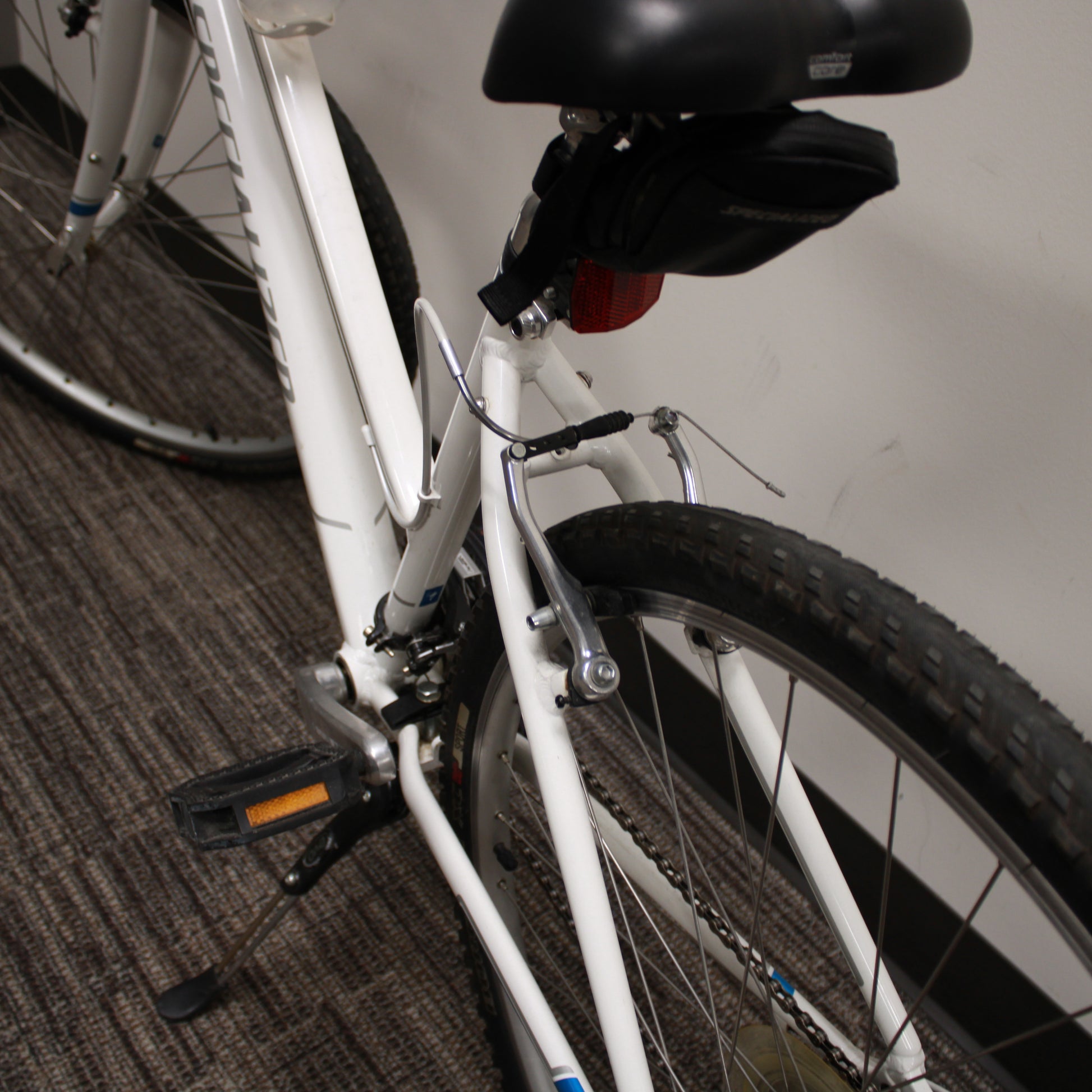 Close-up of a white bicycle with black seat on a carpeted floor.