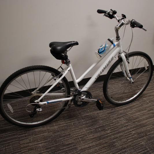 White bicycle with black seat and tires on a carpeted floor against a plain wall.