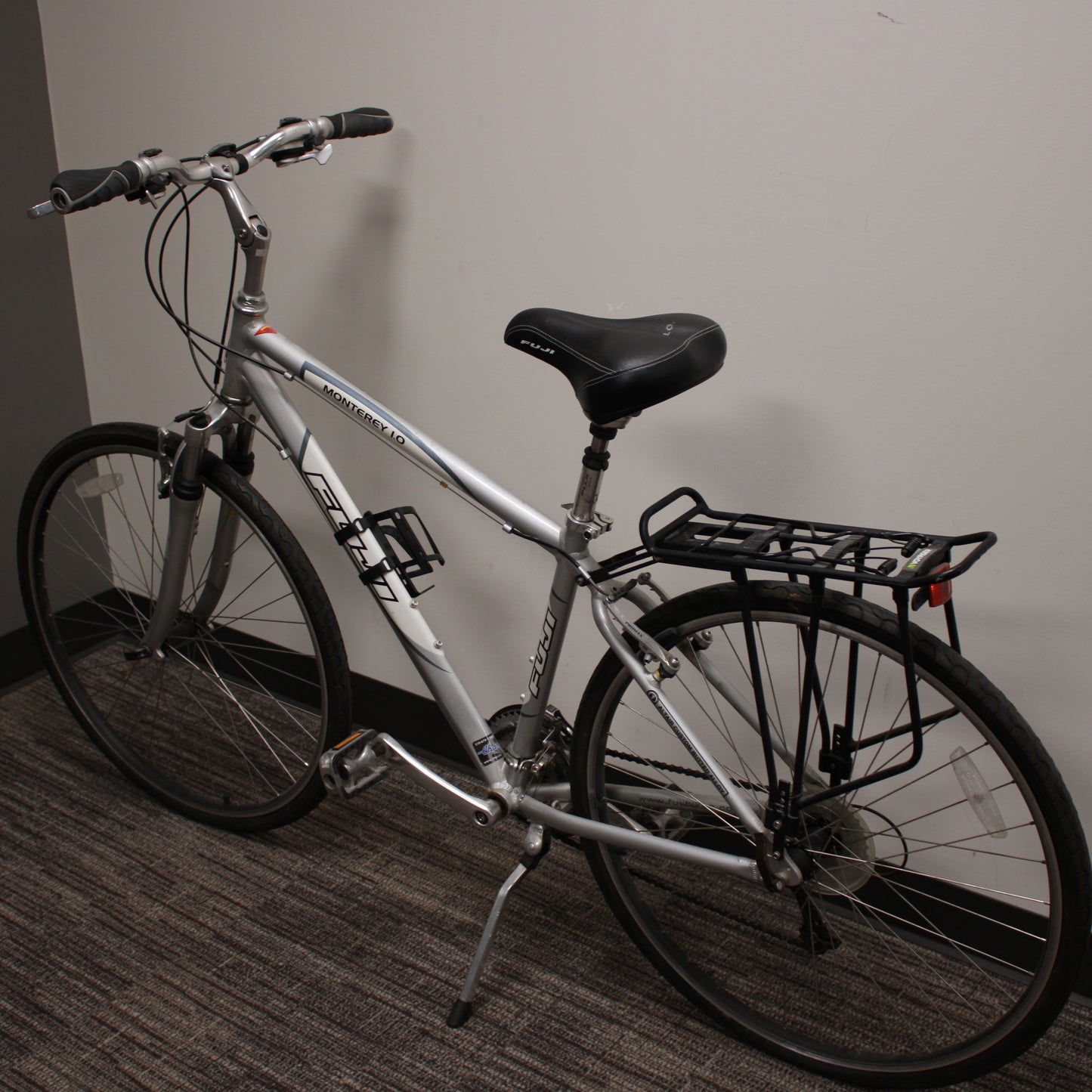 Silver bicycle with a black seat and basket against a plain wall.