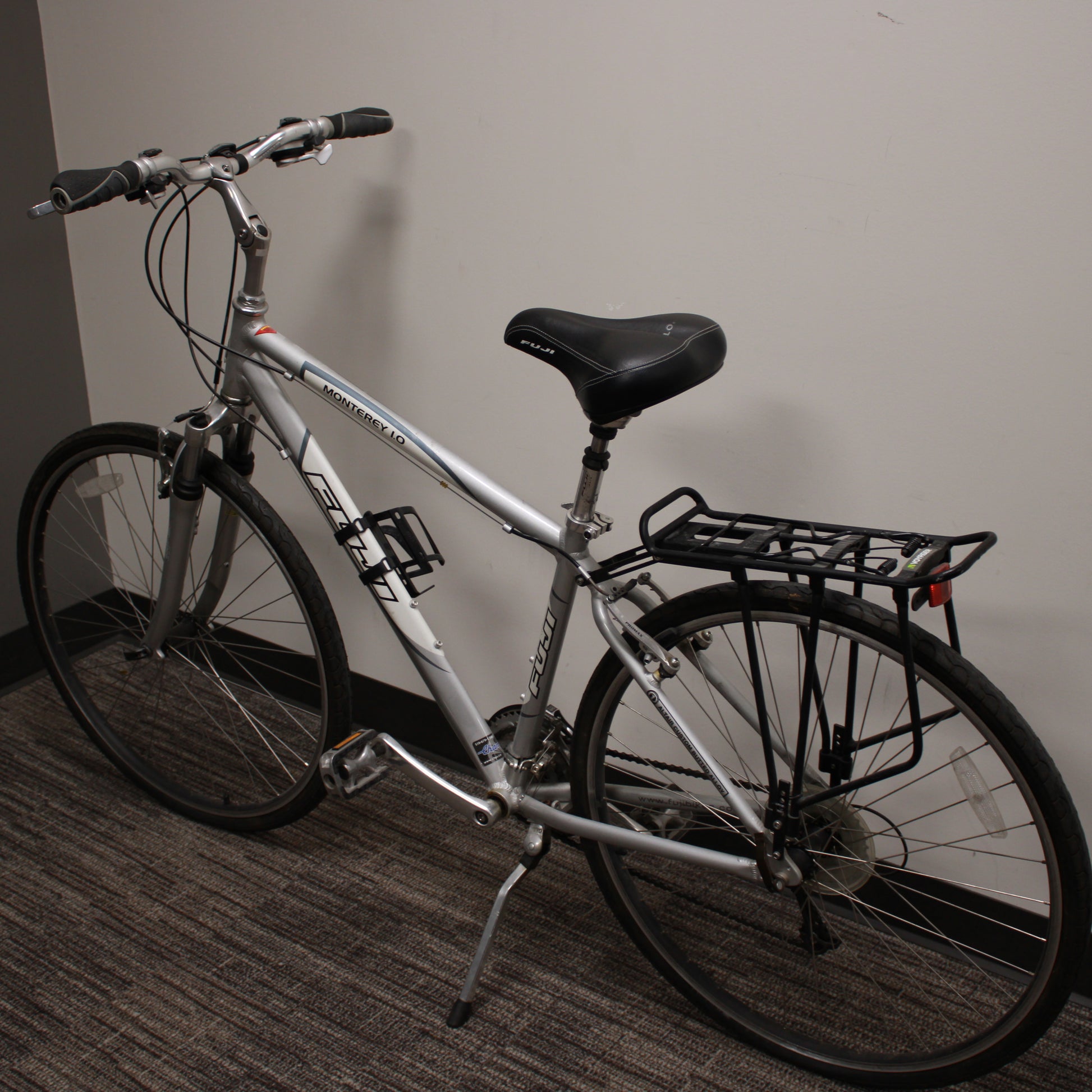 Silver bicycle with a black seat and basket against a plain wall.
