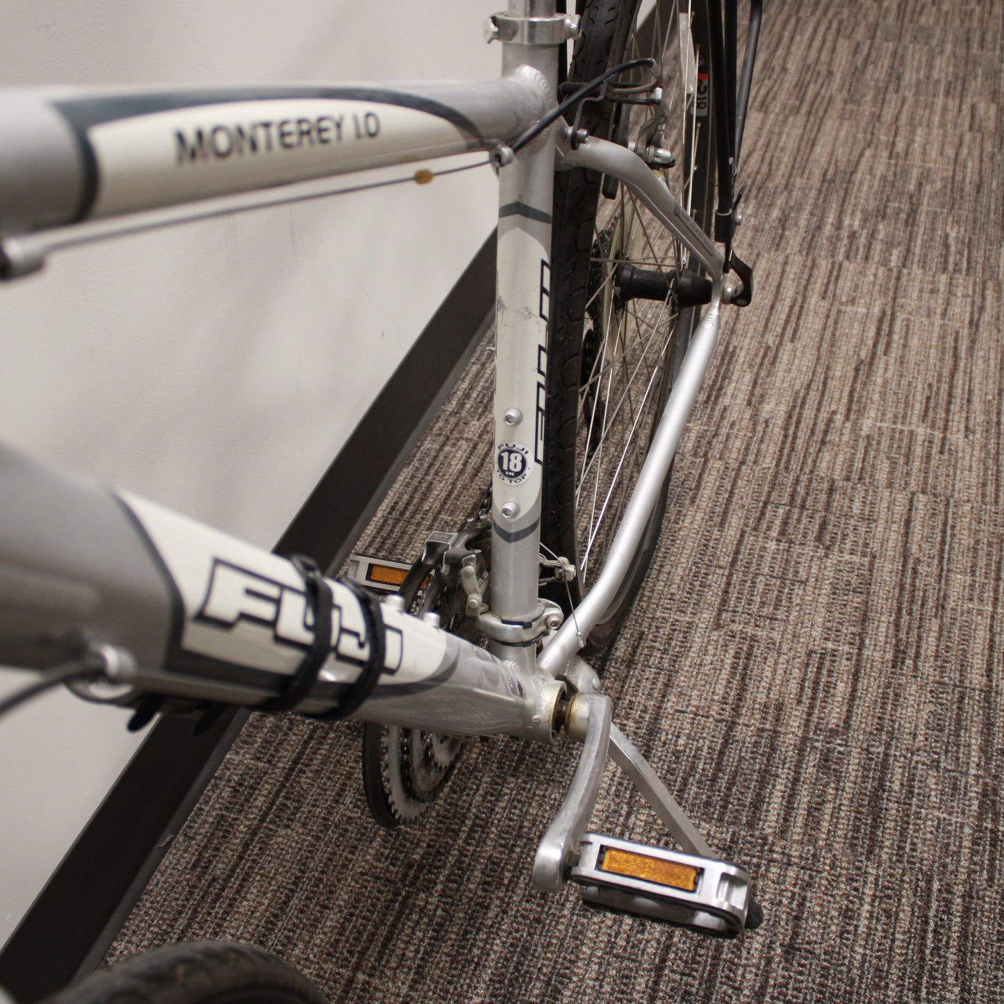 Silver bicycle with a black seat and basket against a plain wall.