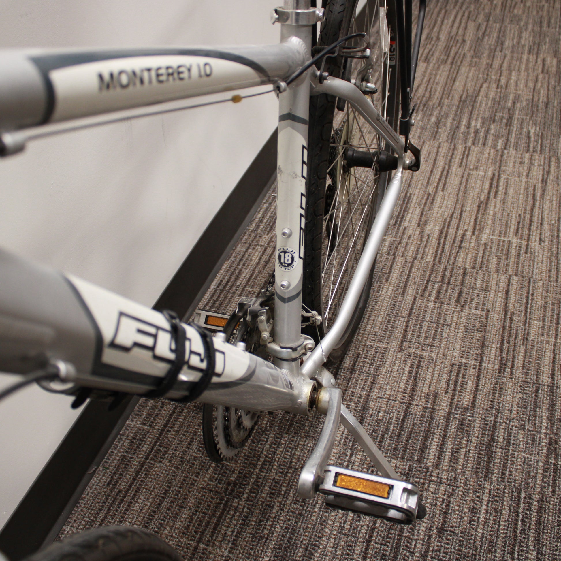 Silver bicycle with a black seat and basket against a plain wall.