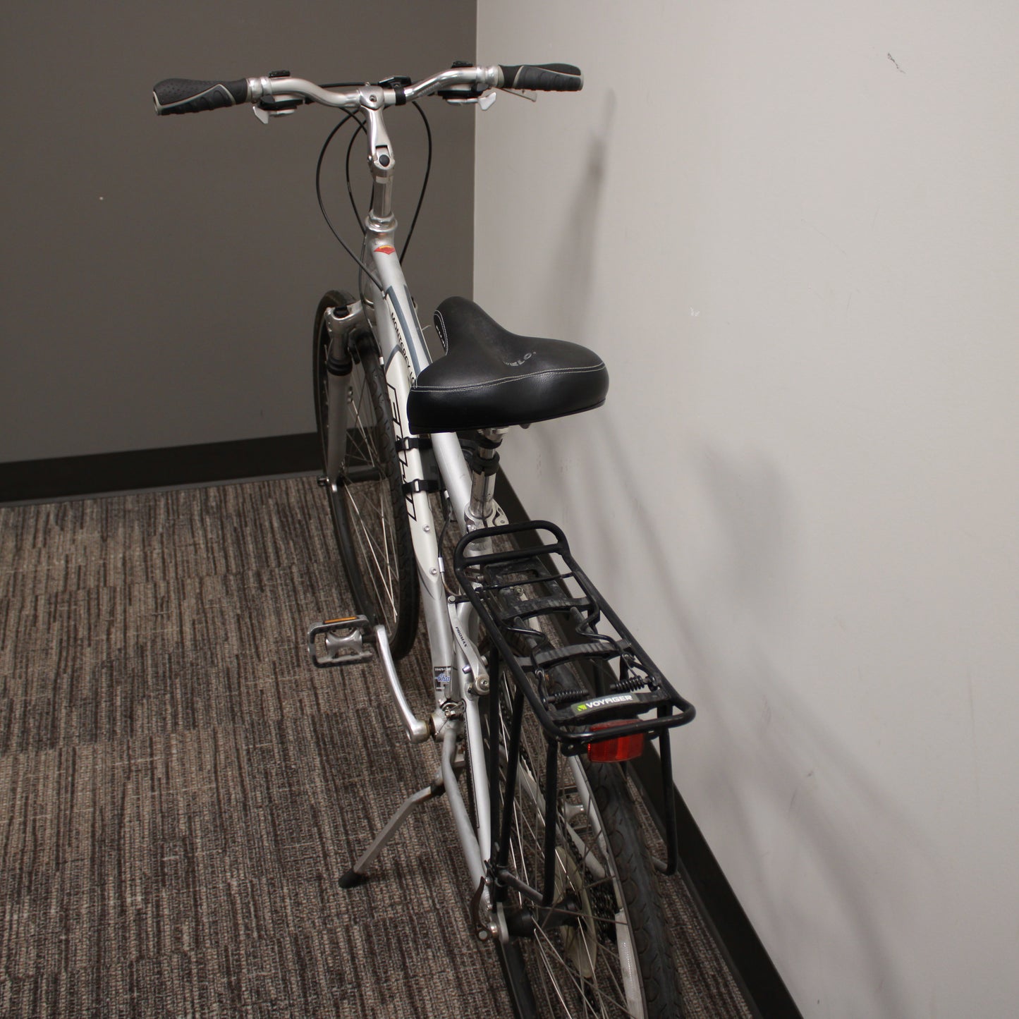 Silver bicycle with a black seat and basket against a plain wall.