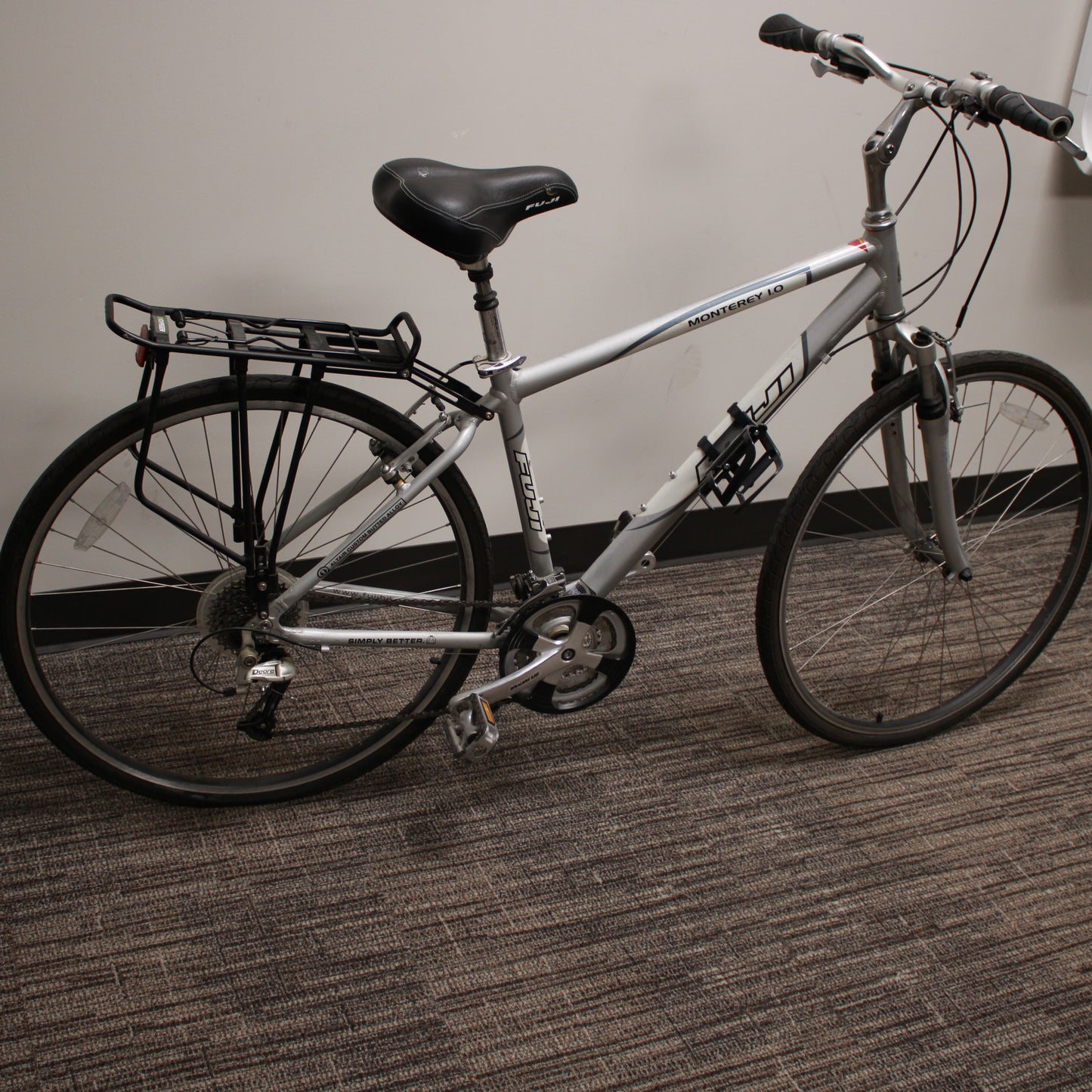 Silver bicycle with a black seat and rear rack on a carpeted floor.