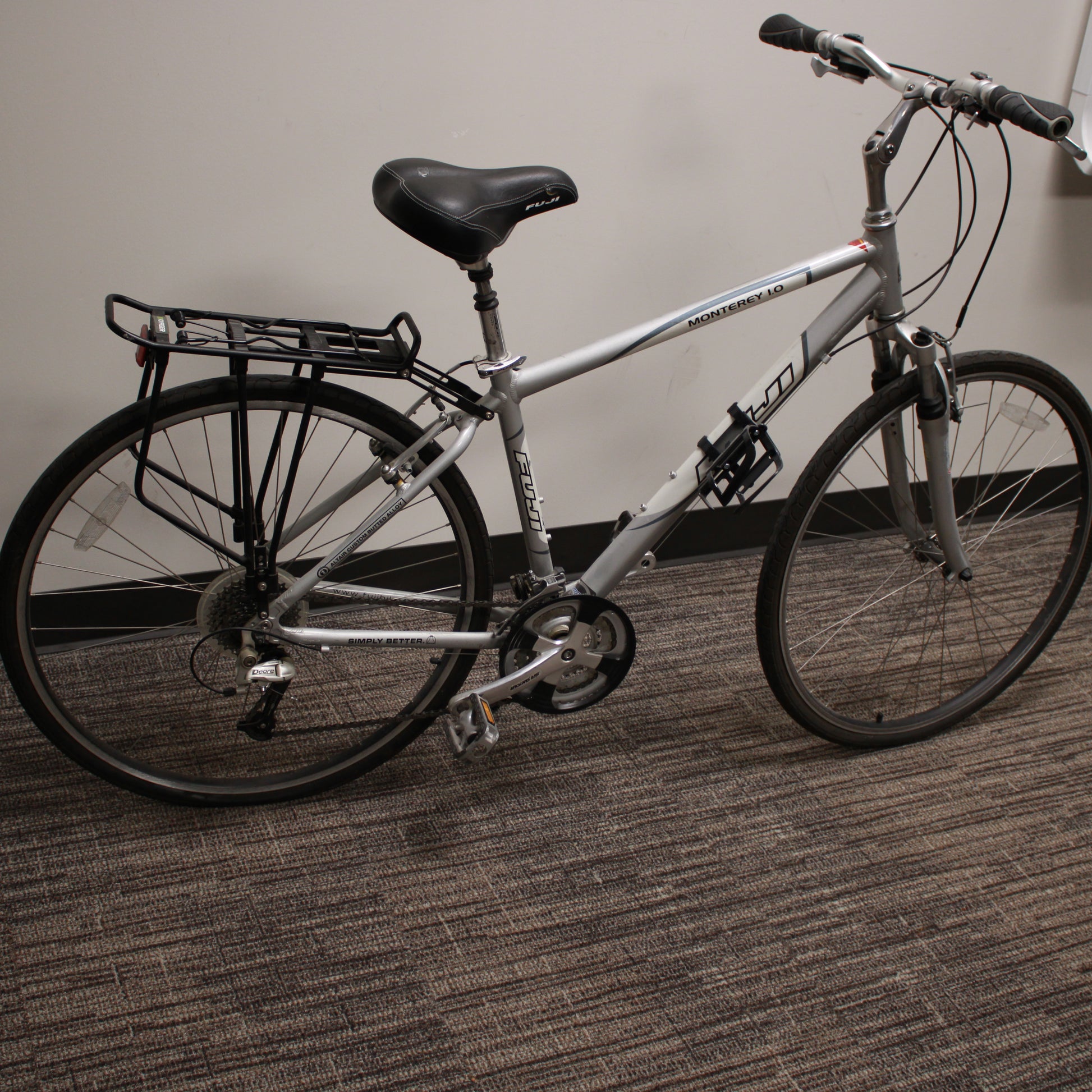 Silver bicycle with a black seat and rear rack on a carpeted floor.