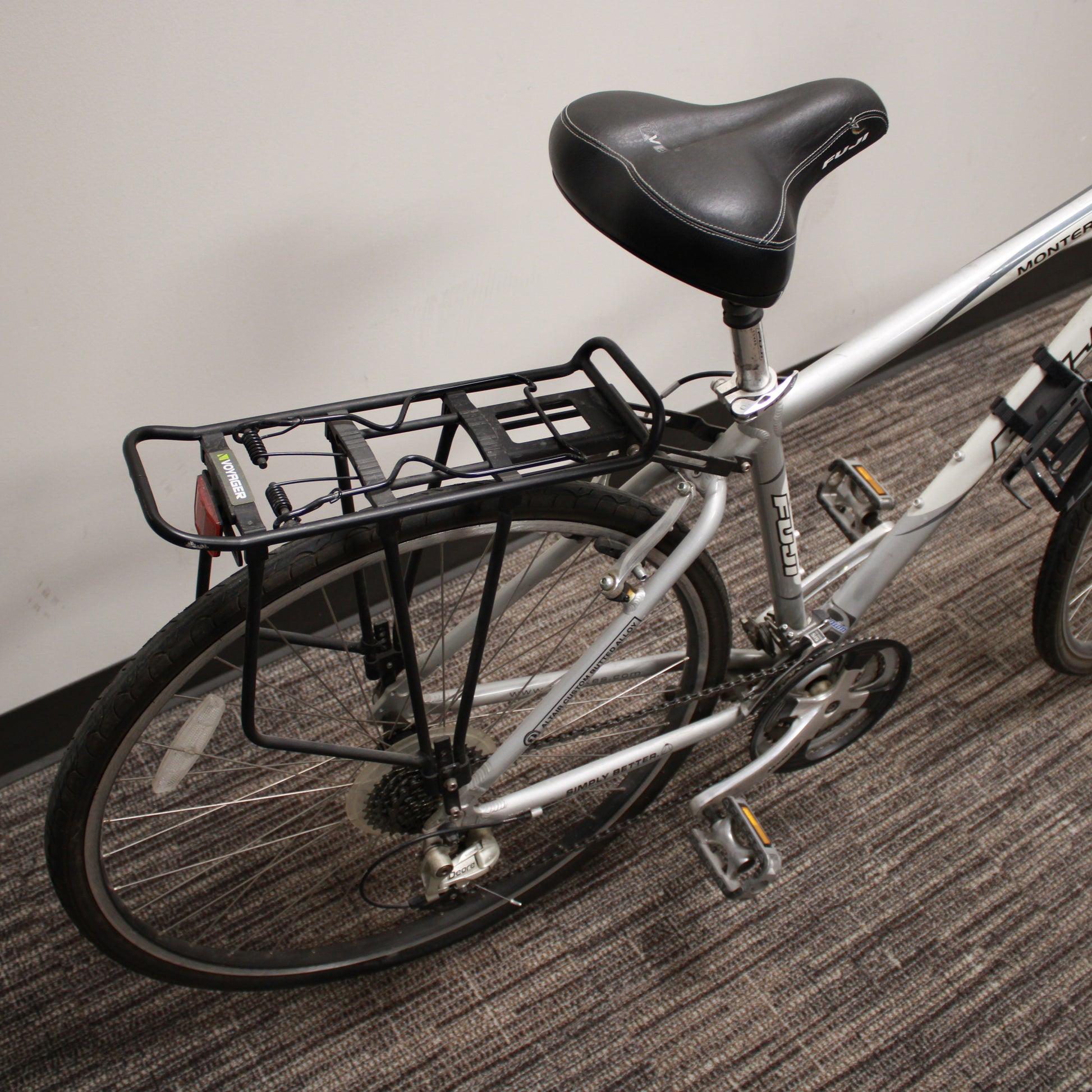 Bicycle with a black seat and rear rack on a carpeted floor.